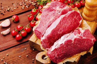 Sulu sığır eti parçaları taze kiraz domatesleri ve baharatlarla çevrili ahşap bir kesim tahtasının üzerinde düzenlenir. Sıcak renkler canlı ve iştah açıcı bir görüntü yaratır. Yemek pişirmek için idealdir..