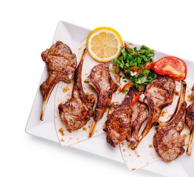 Lezzetli kuzu pirzolaları, taze bitkiler, limon dilimleri ve canlı domateslerle birlikte bir tabakta güzelce düzenlenir. Bu yemek her et sever için mükemmeldir..