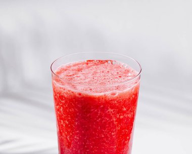 Beyaz bir masada duran ferahlatıcı bir çilekli smoothie ile uzun bir bardak.