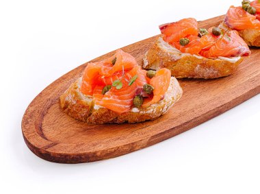 Taze hazırlanmış somon bruschetta ahşap bir tabakta güzelce düzenlenmiştir. Tabakta lezzetli somonla kaplanmış ve kapari ile süslenmiş ekmek dilimleri yer alıyor..