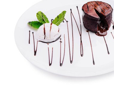 Bozulmuş çikolatalı lav keki, yanında bir top vanilyalı dondurma ve taze nane yapraklarıyla birlikte beyaz bir tabakta duruyor. Çiselemiş çikolata sosu zarafet katar..