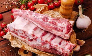 Taze domuz kaburgaları sarımsak ve canlı domateslerle çevrili bir parşömen parçasının üzerinde oturur. Lezzetli bir yemek hazırlığı için gerekli malzemeler sergilenir..