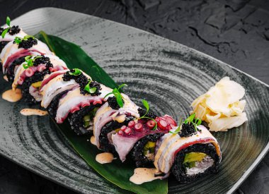 Görsel olarak cezbedici bir suşi rulosu siyah pirince sarılmış taze balık ve sebze katmanlarına sahiptir. Zarif garnitürler havyar ve zencefil içerir. Hepsi koyu dokulu bir tabakta dizilmiştir..