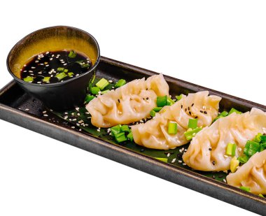 Bir tabak, doğranmış yeşil soğan ve susam tohumlarıyla süslenmiş buharlı hamur köfteleri içeriyor. Küçük bir kase lezzetli bir sos içerir, lezzet katar..