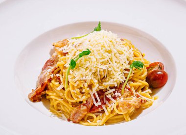 Bir tabak spagetti tabağı, üzerinde çıtır pastırma, kiraz domatesleri ve lezzet için taze otlarla süslenmiş bol miktarda rendelenmiş peynir içeren altın makarna içerir..