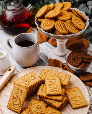 Çok güzel hazırlanmış bir kurabiye çeşidi bir fincan buharlı çayın yanında bir masada oturur. Taze pişmiş ikramlar sanatsal bir şekilde sunuluyor, herkesi eğlenmeye davet ediyor..