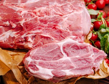 Çiğ domuz eti, olgun domatesler ve taze yeşilliklerle birlikte kahverengi kasap kağıdında sergileniyor. Hazırlanan malzemelerin canlı renklerini ve dokularını vurguluyor..