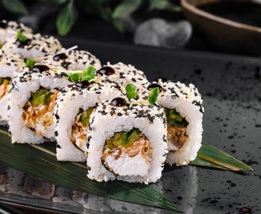Gourmet sushi rolls with sesame seeds served on a bamboo leaf with chopsticks