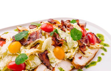 Renkli bir salatada çıtır pastırma, kiraz domatesleri ve taze sebzeler bulunur. Bu yemek büyük beyaz bir tabakta servis edilir, canlı bileşenlerini vurgular..