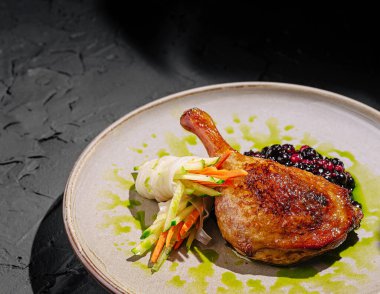 Renkli sebzeler ve zengin böğürtlen sosuyla süslenmiş güzel bir ördek bacağı. Çanak desenli siyah bir arkaplana karşı ayarlanmış, canlı renklerini vurguluyor.