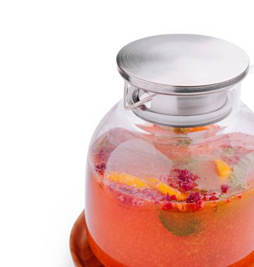 Dilimlenmiş meyvelerle dolu renkli içecek cam bir kavanozda duruyor. Karışımda buz ve parlak gümüş kapaklı ahududu yer alıyor..