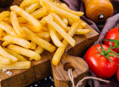 İştah açıcı altın patates kızartması, yanında olgun domateslerle birlikte, ahşap tahta üzerinde servis edilir.