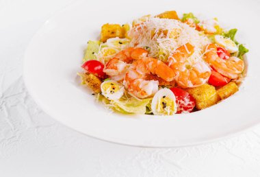 Lezzetli karides, kıtır marul, kıtır ekmek ve beyaz arka planda parmesanlı sezar salatası.