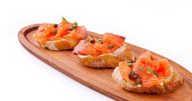 Taze somon füme ve kapari ile kaplı üç parça kızarmış ekmek ahşap bir tahtanın üzerinde zarif bir şekilde düzenlenir. Toplamak için mükemmel bir gurme aperatifi sergilenir..