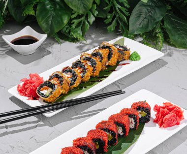 Beyaz tabaklarda iki çeşit suşi rulosu sergileniyor. Wasabi ve zencefil turşusuyla güzelce süslenmiş. Canlı sunumu tamamlayan küçük bir tabak soya sosu..
