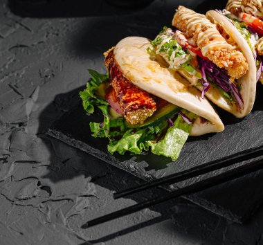 Siyah tahta tabakta gevrek dolgular, taze marul ve renkli lahana salatasıyla dolu enerjik tacolar var. Tacolar sanatsal bir şekilde düzenlenmiş, çeşitli dokuları ve tatları cezbedici bir şekilde gösteriyor..