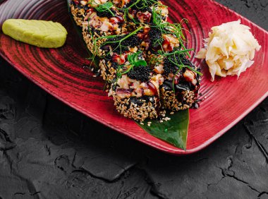 Renkli malzemelerle süslenmiş, wasabi ve turşulu zencefil turşusuyla süslenmiş çeşitli suşi rulolarının yer aldığı canlı kırmızı bir tabakta güzel bir suşi servis edilir..