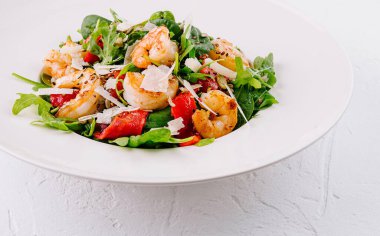 Beyaz tabakta roka, parmesan ve çilekli taze karides salatası.