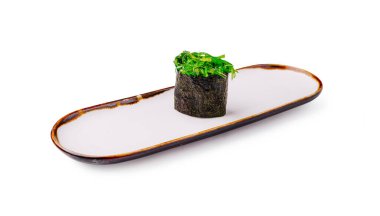 Bir suşi rulosu basit beyaz bir tabakta sunulur, içinde yosun ve narin yeşil malzemeler bulunur. Düzenleme, taze malzemeler ve mutfak sanatının odak noktasını vurguluyor.