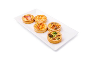 Beyaz servis tabağında çeşitli lezzetli turtalar düzgünce düzenlenir. Her turtanın farklı dolguları vardır. Yumurta, sebze ve et gibi gösterişli tatları vardır. Brunch veya aperatif için mükemmeldir..