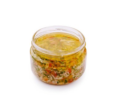 Canlı yağ ve ince doğranmış sebzelerle dolu cam bir kavanoz düz bir yüzeyde duruyor. Karışımda bitkiler var ve taze aromalı yemekleri geliştirmek için idealdir..