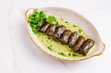 Doldurulmuş üzüm yaprakları canlı yeşil sos ve taze otlarla kaplı bir tabakta zarif bir şekilde sıralanmış gibi görünüyor. Bu yemek leziz bir lezzet ve doku karışımı sergiliyor..