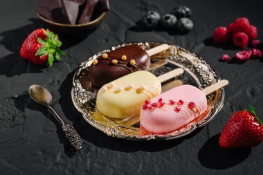 Çikolata, vanilya ve çilek aromalı üç lezzetli dondurma süslü gümüş bir tepside düzenlenir. Taze çilek, ahududu ve yaban mersini ziyafeti tamamlar..