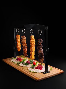 Terbiye edilmiş et şişleri taze sebze ve otlarla birlikte ahşap bir tabakta sunuluyor. Paylaşım için mükemmel renkli bir mutfak görüntüsü.