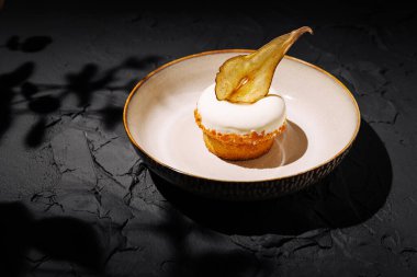 Baştan çıkarıcı bir tatlı, dokulu bir tabakta sunulur, üzerinde kremalı beyaz krema ve dekoratif armut dilimi olan nemli bir kek sergilenir, tatlı bir hoşgörü için mükemmeldir..