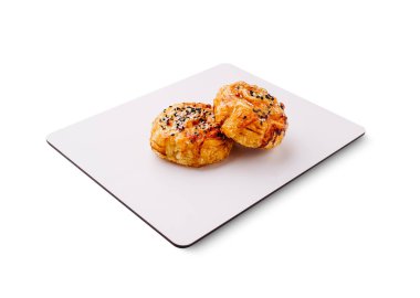 Üzerinde susam tohumları olan iki altın sarısı hamur işi beyaz bir tepside oturur. Pul pul olmuş ve taze pişmiş görünüyorlar. Atıştırmalık ya da tatlı için ideal..