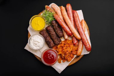 Ahşap bir tabakta çeşitli ızgara sosisler düzenlenir. Yanında da hardal, sos ve kremalı sosun yanında taze lahanalar ve ekşi lahana turşusu var..