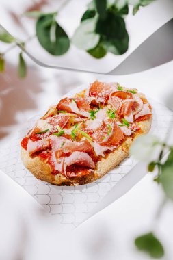 Bir yassı ekmek zarif bir şekilde pişirilmiş et, ot ve peynir katmanlarıyla, canlı renkler ve dokularla hazırlanır. Sunumda aşçılık sanatı ve tazeliği vurgulanıyor.