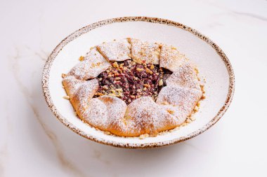 Yuvarlak bir tatlı, fındık ve tatlı karışımı ile doldurulmuş, pudra şekerli. Ödül dekoratif seramik tabakta sunuluyor..