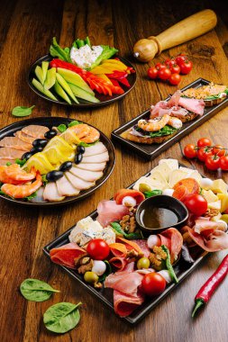 Ahşap masada sergilenen lezzetli mezeler arasında karides, soğuk et, peynir, biber, domates, zeytin ve taze sebzeler yer alıyor. Sosyal toplantı ya da parti için ideal..