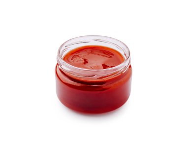 Küçük cam bir kavanozda kalın, canlı kırmızı bir sos var. Sos pürüzsüz bir dokuya sahiptir, bu da onu çeşitli mutfak yemekleri için ideal kılar. Basit ve net bir arkaplanda oturuyor, rengini vurguluyor..