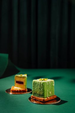 İki karmaşık yeşil tatlı, altın tabakların üzerinde koyu bir zemine karşı zarif bir şekilde otururlar. Tatlı ikramlar, hoşgörüyü teşvik eden pürüzsüz bir dış ve zengin dolguları içerir..