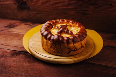 Yuvarlak, taze pişmiş bir pasta ahşap bir tahtanın üzerinde, zengin, davetkar bir dokuya sahip altın bir kabuk sergiliyor. Odunların ılık tonları cazibesini arttırır. Her toplanma için mükemmeldir..