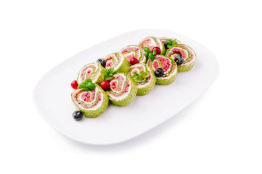 Canlı sebze dürümleri beyaz bir tabakta düzgünce sıralanır, yeşillik katmanları, dolgular ve taze bitki ve böğürtlenlerle süslenir, büyüleyici bir sunum oluşturur..