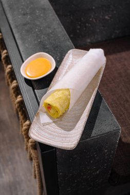 Taze malzemelerle dolu bir börek küçük bir sos tabağının yanında duruyor. Modern dekor yemek deneyimine biraz zarafet katıyor..