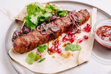 Lezzetli ızgara kebap taze kişniş, nar tohumu ve dilimlenmiş soğanla kaplıdır. Yanında da küçük bir kase keskin sos vardır. Lezzetli bir yemek için mükemmeldir..