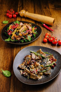 Kırsal siyah tabaklarda sunulan canlı bir gurme ikilisi. İlk tabakta susamlı Asya usulü rengarenk kızartılmış sebze salatası, ikincisinde ise kremalı tavuk ve siyah susam var.