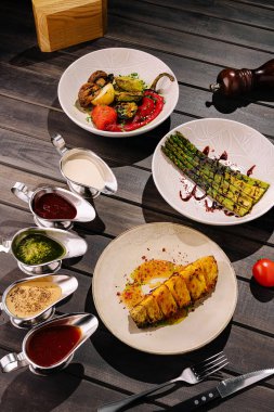 Cezbedici bir vejetaryen tabağı ızgara sebzeler ve ahşap bir masada ustalıkla hazırlanmış çeşitli soslar sergiliyor. Taze malzemeler canlı renklerini ve tatlarını vurgular.