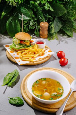 Taze sebzeler, çıtır patatesler ve bir kase sıcak çorbayla süslenmiş vişneli domatesler ve yapraklı yeşilliklerle sulu bir hamburger içeren canlı bir yemek..