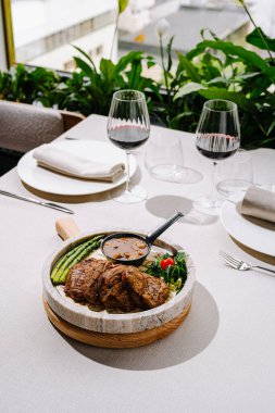 Çağdaş bir restoranda, yanında kırmızı şarap ve kuşkonmaz eşliğinde güzel bir ızgara biftek tabağı sunuluyor ve muhteşem bir yemek deneyimi sunuluyor..