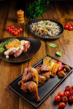 Ahşap bir masaya üç güzel kaplanmış gurme tabağı konur. Bir tanesi kızarmış tavuk, diğeri renkli salata ve sonuncusu da taze domateslerle tamamlanmış et yemeği sunuyor..