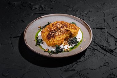 Karnabahar bifteği, ezilmiş fındıkla kaplı ve canlı soslarla çevrili dokulu bir tabakta güzelce sunuluyor..