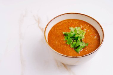 Renkli sıcak bir mercimek çorbası taze yeşil otlarla kaplıdır. Kırsal kase beyaz mermer bir yüzeye dayanır, sıcaklığı ve rahatlığı davet eder..