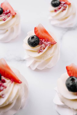 Enfes mini tatlılarda çilek ve yaban mersinli kremalı girdaplar bulunur. Aydınlık bir yüzeye mükemmel bir şekilde yerleştirilmişler. Kutlamalar için cazip ve tatlı bir ikram sunuyorlar..