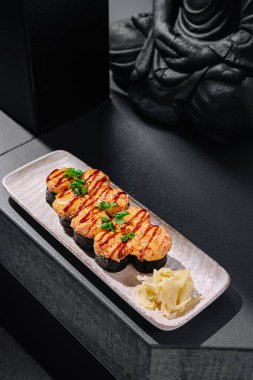 Üzerinde deniz mahsulleri ve çiselemeli sos bulunan güzel düzenlenmiş bir suşi tabağı. Yanında da turşu turşusu ve dingin bir zemin..