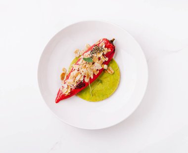 Lezzetli malzemelerle dolu canlı bir kırmızı biber pürüzsüz bir yeşil sosun üzerinde oturur. Dilimlenmiş bademlerle süslenmiş yemek, iştah açıcı ve renkli görünüyor. Mutfak zevki için ideal..